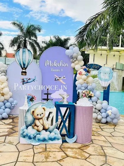 A stunning hot air balloon and teddy bear themed first birthday set up by a swimming pool. The pastel blue decor contrasts beautifully with the water.