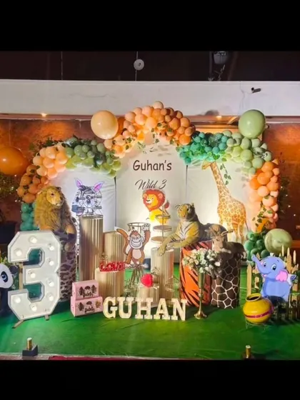 We created a complete jungle safari for Guhan's third birthday. The decor includes large animal props like a lion, tiger, and giraffe, along with a balloon arch in earthy tones and a personalized "Wild 3" backdrop.