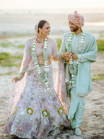 A lovely, candid shot of the couple walking on the beach after their ceremony, dressed in beautiful pastel wedding outfits.