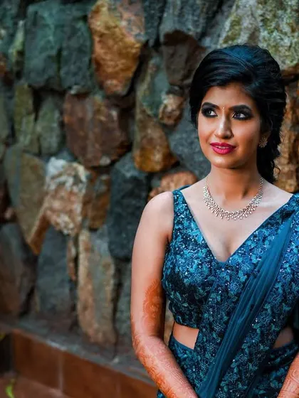 A quiet, thoughtful portrait of the bride against a rustic stone wall, showcasing her blue sequined lehenga in a different light.