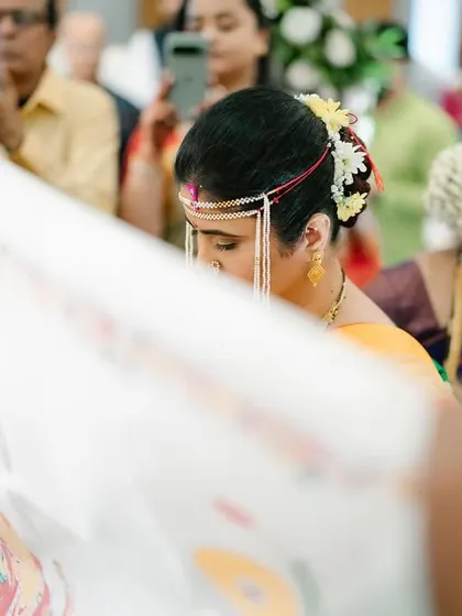 A candid shot of the bride during the Antarpat ceremony. The focus is on her as she peeks from behind the cloth, capturing a moment of quiet anticipation.