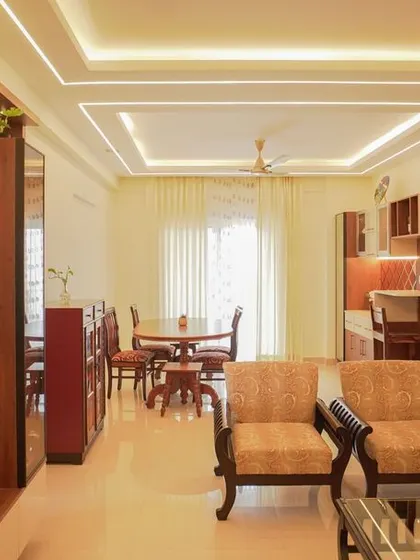 This traditional living and dining space features classic wooden furniture and a cohesive design flow. The TV unit is framed by a wooden structure, and a multi-level false ceiling with profile lighting connects the entire area.
