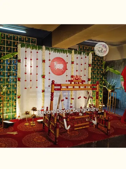A simple and elegant naming ceremony decor. The backdrop features jasmine and rose garlands, with a traditional cradle ready for the baby. The red cloth for the name reveal adds a pop of color.