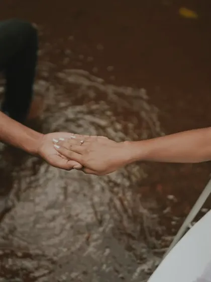 An artistic and symbolic shot of a couple holding hands while seated in chairs surrounded by water. This conceptual photo is about connection and trust.