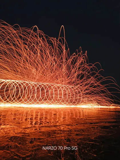 A long exposure shot using steel wool to create light trails on a beach at night. This photo, taken on the Narzo 70 Pro 5G, showcases creative low light photography techniques.