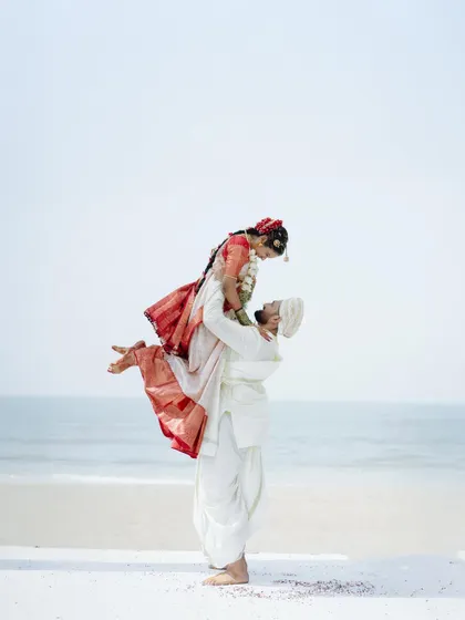 A playful and romantic beachside portrait, with the groom lifting his bride into the air against the ocean backdrop.
