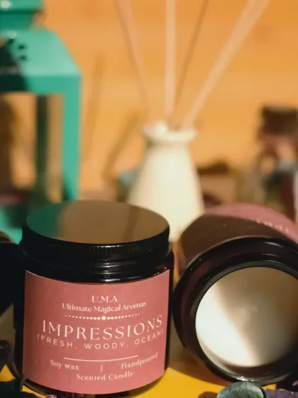 A pair of 'Impressions' candles, one open and one closed. This fragrance is perfect for when you want to impress guests with a home that smells cozy and positive.