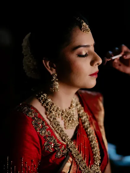 A dramatic, beautifully lit shot of the bride getting her final touches. The classic red lip and gold eyeshadow are hallmarks of a timeless bridal look.