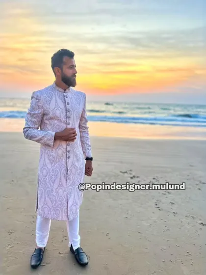 A client looking dapper in our light-colored, intricately patterned sherwani against a beach sunset. This shows how versatile our traditional wear can be, perfect even for a destination wedding.