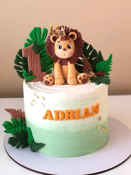 A regal lion-themed cake for a first birthday, with a handcrafted lion king topper and lush jungle leaves.