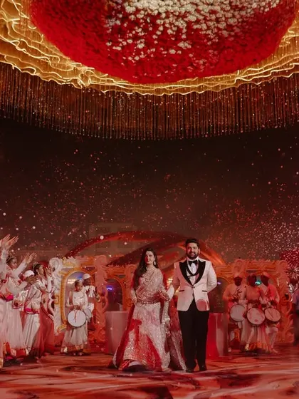 A moment of pure grandeur. The couple makes their way through a sea of dancers and confetti, with the entire venue lit up to celebrate their arrival.