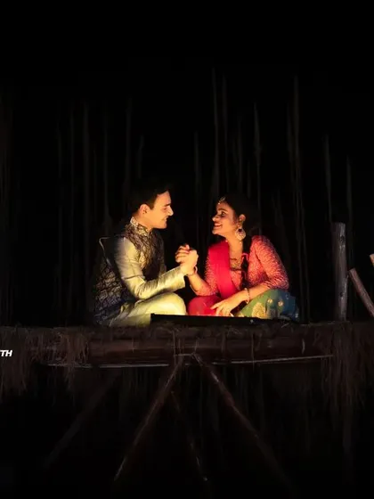 A low-light, intimate shot of a couple in traditional attire. The scene is lit only by two lanterns, creating a very rustic and romantic feel.