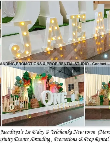 A lovely giraffe theme for a first birthday at Yelahanka New Town. The stage setup features a backdrop with a green and orange balloon garland, a large "ONE" table, and marquee letters, creating a grand and festive look.