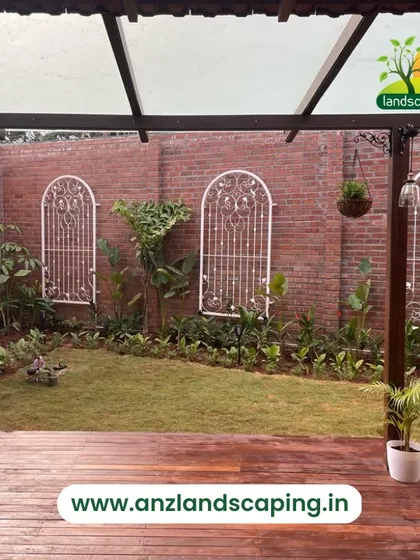 A view from the wooden deck of this villa backyard, looking onto a fresh lawn bordered by a brick wall with decorative white metal trellises.