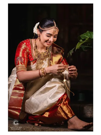 A candid moment of Priyanka getting ready. Her makeup is soft and understated, perfectly matching the elegance of her classic red and white Kanjivaram saree and traditional temple jewelry.