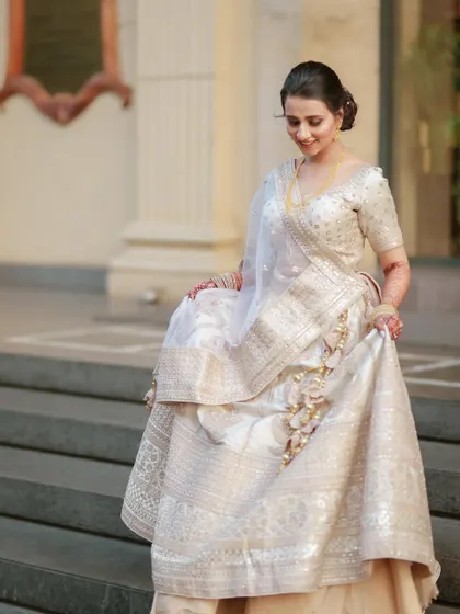 An elegant bride in a stunning white and gold lehenga, captured as she descends the stairs.