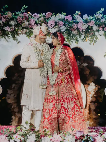 A classic portrait of the bride and groom on the varmala stage, surrounded by a beautiful floral arch. Their smiles and eye contact convey their happiness and deep connection.