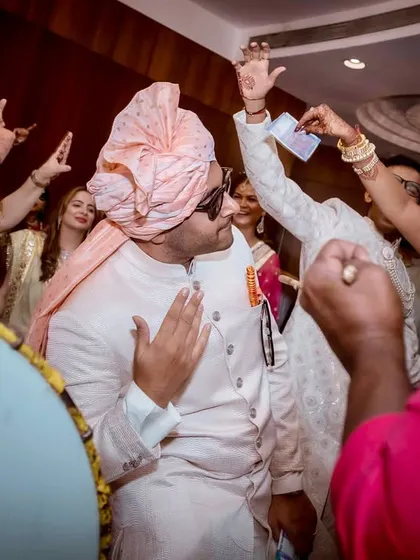 The groom is surrounded by dancing family and friends, all showering him with love and money in the traditional Baraat style.