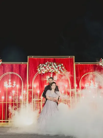A dreamy reception moment for the couple, enveloped in a cloud of low fog and framed by sparklers against a rich red backdrop.