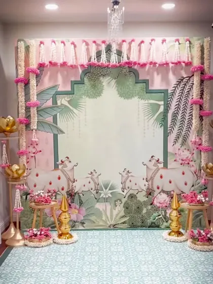A stunning traditional setup for a baby shower or naming ceremony. The Pichwai-inspired backdrop with cows, lotuses, and a pink and green palette is a true work of art.
