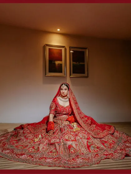 A grand, full-length portrait of the bride Vanshika, seated with her magnificent red lehenga spread out around her, looking like a queen.