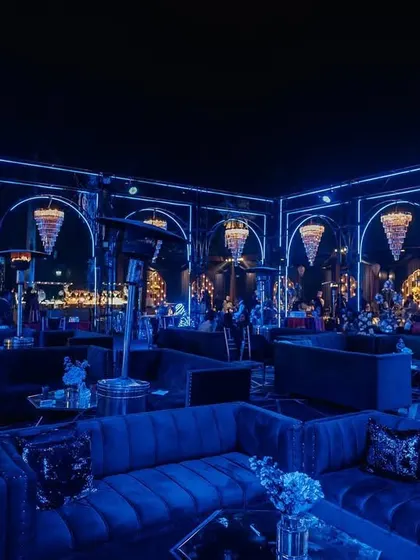 A stunning Sangeet setup with dramatic blue lighting and crystal chandeliers. The plush velvet seating and moody ambiance create a luxurious and glamorous party setting.