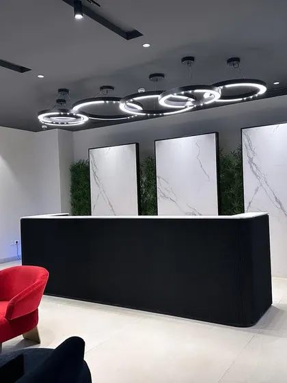 A view of the reception at the ALP Overseas Experience Center in Kota. The modern ring chandelier and minimalist desk are contrasted by a single, bold red armchair, adding a pop of color and personality.
