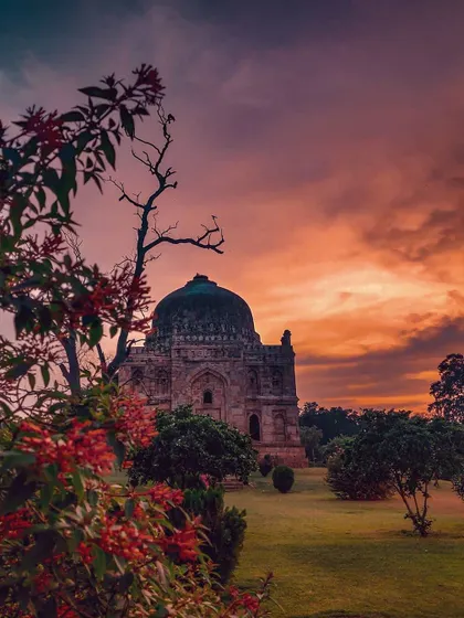 A historic tomb is framed by vibrant foliage against a dramatic sunset sky. This architectural travel photo perfectly balances natural beauty with historical grandeur.