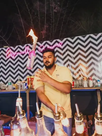 A flair bartender executes a stall, balancing a flaming bottle on his shoulder. This move requires precision and is a highlight of our fire shows.