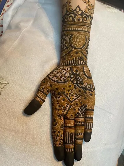 A close-up of an engagement bride's henna, showing the intricate detail on the palm. The design features a central mandala surrounded by fine-line work.