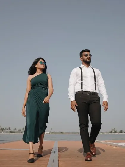 A stylish couple walks confidently along a pier, set against a clear blue sky. This image showcases a modern, chic approach to pre-wedding photography.