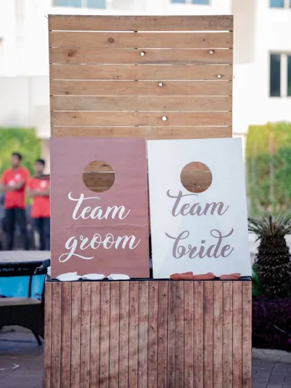 A classic 'Team Bride' vs 'Team Groom' cornhole game, adding a touch of friendly competition and fun to the pre-wedding festivities.