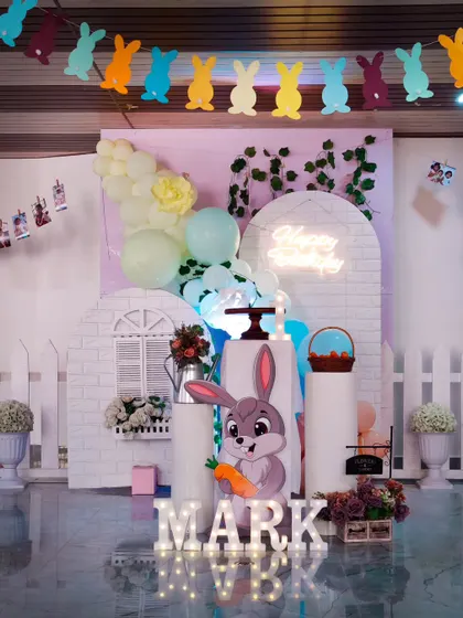 A sweet Bunny Farm birthday theme. This setup uses a white picket fence, a bunny cutout, and pastel balloons to create a cute and charming party.