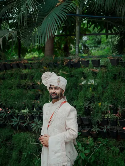 A full-length portrait of the groom standing confidently against a lush green background. His traditional attire and calm demeanor make for a very regal and handsome photograph.