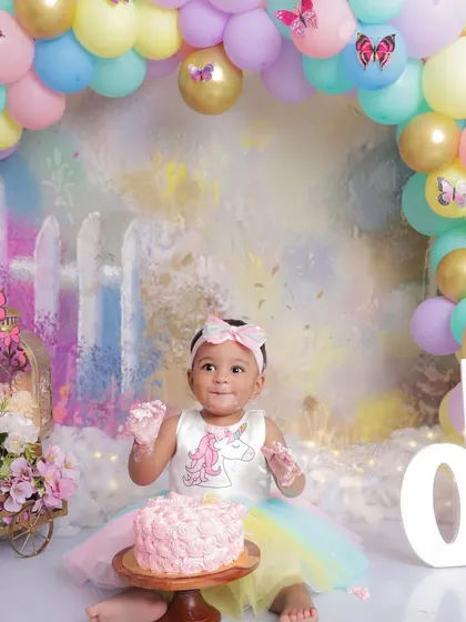 A sweet and slightly messy smile from the birthday girl. This photo captures the fun of a cake smash session, with a beautiful pastel garden backdrop and a colorful balloon arch.