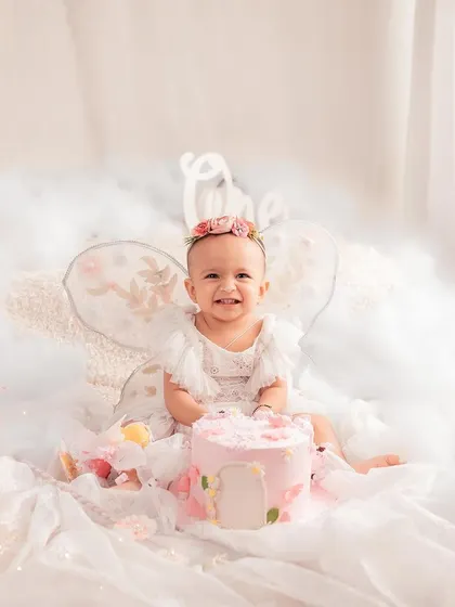 A fairy-themed first birthday cake smash. This sweet girl with her tiny wings, sitting in a bed of clouds with her pink cake, looks like she's straight out of a storybook.