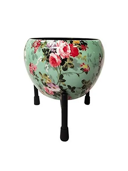 This is our Green Meena Apple Pot, featuring a lovely floral design on a mint green background. The metal pot comes with a stand, making it a stylish and complete decor piece.
