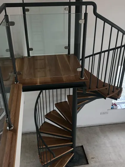 The landing detail, showing the solid oak tread with walnut inlay and the connection to the glass balustrade on the upper level.