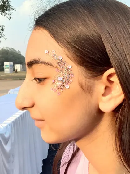A beautiful crescent of pink glitter and sequins along the temple. This is a very popular and trendy festival look.