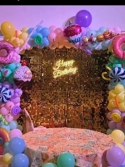 A candy-themed party with a gold sequin backdrop and a balloon arch featuring large donut and cupcake foil balloons.