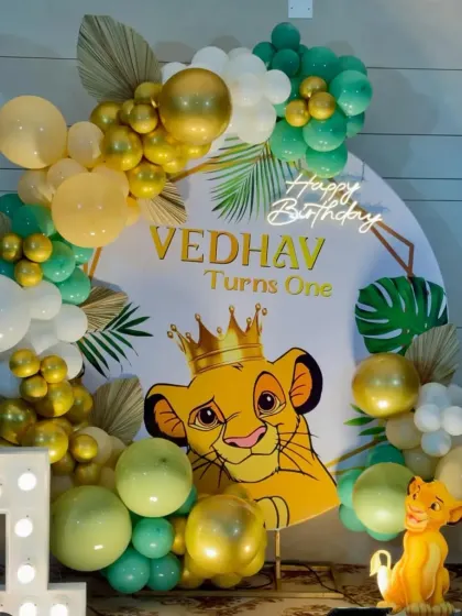 A cute Simba-themed first birthday with a character backdrop, a "1" marquee number, and a balloon arch in green, yellow, and gold.