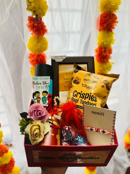 A Rakhi gift hamper in a red box, personalized with a photo frame and a "Thanks for always being by my side" sticker.