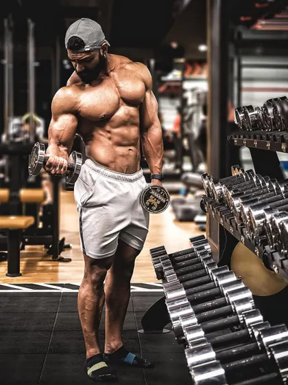 Performing a concentration curl next to the dumbbell rack. This exercise is excellent for isolating the bicep and building a prominent peak.