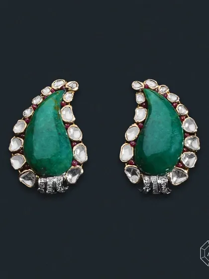 These emerald earrings feature large drop-shaped emeralds complemented by uncut diamonds, round diamonds, and baguette diamonds.