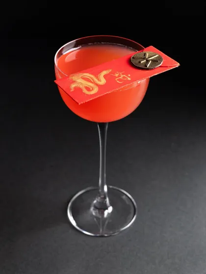 A striking red cocktail with a Chinese New Year-themed garnish, shot against a black background to make the color pop.