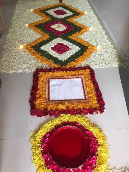 We specialize in detailed floral floor art, known as rangoli. This piece features intricate geometric patterns created with fresh petals of marigold, rose, and jasmine, with small diyas placed to add a warm glow.