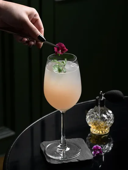 A beautifully garnished gin-based cocktail, with edible flowers and a spritz of perfume, showcasing my attention to detail.