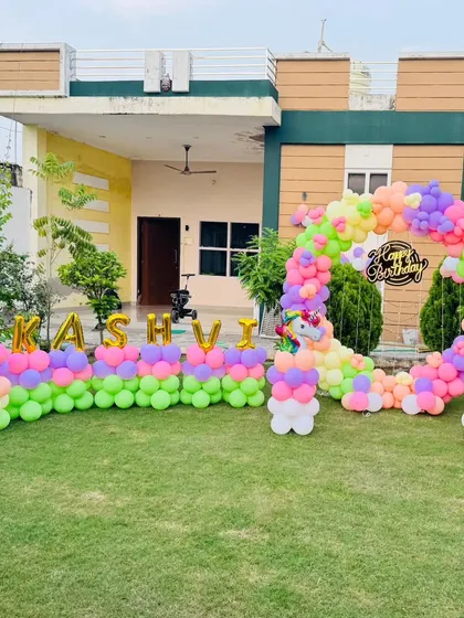 A wide shot of an outdoor unicorn-themed party for "KASHVI". The extensive balloon decoration creates a festive and impressive setup in the home's garden.