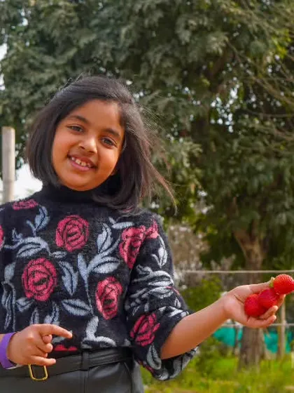 A young girl holds up a bright red radish, a small treasure from her day of harvesting. It's a great photo opportunity and a proud moment for her.
