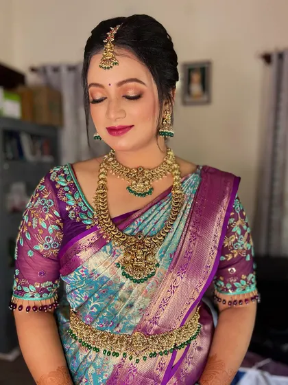 This bride from Mysore looks radiant in a unique peacock-toned silk saree. Her makeup features a soft pink and gold eye look with a matching lip color to complement her intricate floral blouse.